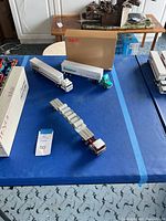 Photo showing three collectible toy trucks on a blue table, including a Mack truck with concrete pipe loads and a white Bowman semi-truck with green cab