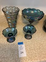 Four iridescent carnival glass pieces displayed on countertop: vase, pedestal bowl, two candle holders
