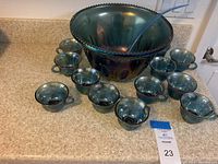 Photo showing the full punch bowl set including the large punch bowl, 12 matching cups, and blue plastic ladle arranged on a kitchen counter.