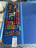 View of 41 assorted vintage toy cars and trucks arranged on a blue surface, showing variety of colors and types, mostly die-cast or metal toys with wear marks