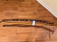 Photo showing three walking sticks side by side on wooden floor, clearly displaying overall length and carved details.