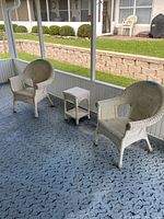Photo of two white wicker chairs and one matching white wicker side table on a screened porch floor