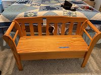 Full view of the wooden storage bench showing slatted backrest and armrests, placed on carpeted floor in a bedroom.