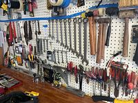 Full view of a garage pegboard with hand tools including wrenches, hammers, screwdrivers, pliers, and painting brushes neatly hung.