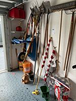 Wide angle showing multiple yard tools including shovels, rakes, flags, wheelbarrow and buckets.