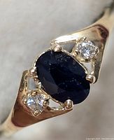 Close-up front view showing oval blue sapphire and two small round diamonds in yellow gold setting.