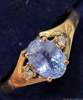 Close-up photo of the ring showing the oval blue tanzanite center stone with two smaller diamonds on each side set in 10K yellow gold.