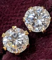 Close-up photo of the pair of round cubic zirconia stud earrings with 10K gold prongs against a textured dark fabric.