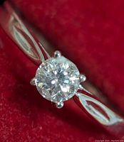 Front-facing close-up of round brilliant diamond in six-prong setting against red background