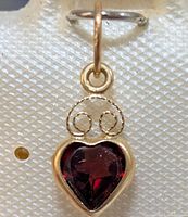 Close-up front view of heart-shaped garnet pendant in gold on white textured display.