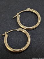 Pair of small polished 14K gold hoop earrings on a black background.