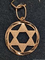 Front view of 18K gold pendant showing broken down Star of David suspended inside a circular frame with twisted edge and oval bail.