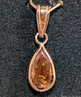 Close-up image of the teardrop-shaped pendant with yellow-brown diamond set in 14K gold on black background.