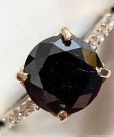 Close-up top view of round faceted black diamond in four-prong setting, white diamond accents on band