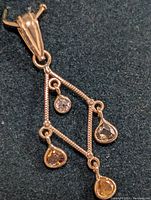 Front view of the geometric pendant showing the four colored diamonds and center white diamond on a textured gold frame.