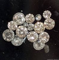 Close-up image of 15 assorted loose diamonds on black background showing sparkly facets and round cuts.