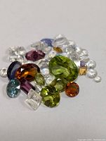 Close-up image showing loose faceted gemstones in a variety of colors including green, purple, aqua, and orange on a white background.