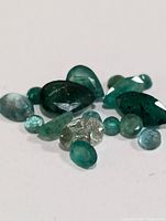 Close-up of various genuine emerald stones with different cuts and green tones against white background