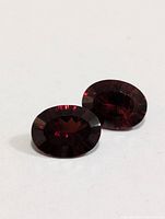Photo of two oval faceted garnet gemstones shown from flat top angle, showing deep red color and facets.