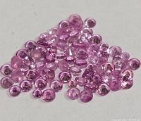 Close-up image showing a pile of small round faceted pink sapphires with a clean reflective surface and consistent pink coloration.