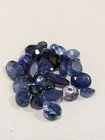 Close-up photo of multiple loose blue sapphires placed on a light surface.