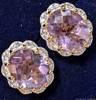Close-up photo showing front view of two oval faceted light purple amethyst earrings with clear stone halo, set in silver and gold-tone prongs.