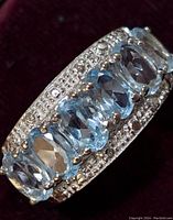 Close-up angled view of silver ring with multiple oval blue topaz stones and small accent clear stones on the band