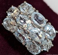 Close-up front view of silver ring showing three rows of oval blue topaz stones set with prongs.