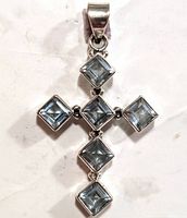 Front view of a silver cross pendant with five square light blue topaz stones set individually in silver and connected to form the cross shape.