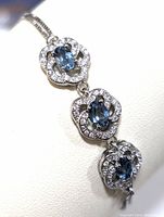 Close-up of three linked floral silver sections featuring oval blue topaz stones surrounded by cubic zirconia