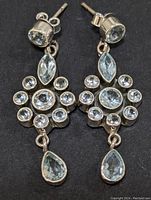 Front view of paired drop earrings showing the silver setting and multiple faceted blue topaz stones in round, marquise, oval, and pear shapes.