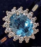 Close-up top view showing oval blue topaz center gem and surrounding clear stones in silver setting.