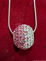 Front view of the pavé cubic zirconia ball pendant showing the pink and clear stones on a silver chain with red velvet background.