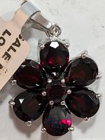 Close-up photo of gem flower-shaped silver pendant with deep red garnets visible in teardrop and round shapes.