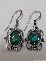 Photo showing front of each earring featuring blue-green faceted oval gemstones set in decorative silver frames.