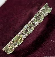 Close-up image of the silver ring showing multiple oval-cut green sapphires set along the band against a dark background.