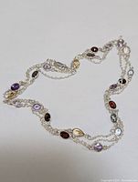 Full view of the silver necklace displaying multiple colored gemstones spaced evenly on a double chain with lobster clasp
