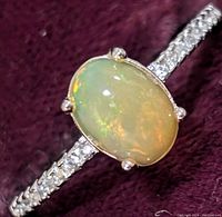 Close-up view of silver ring featuring oval opal center and cubic zirconia accents on the band.