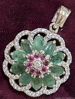 Close-up front view of the silver pendant showing the emerald petals, ruby stones, and cubic zirconia border.