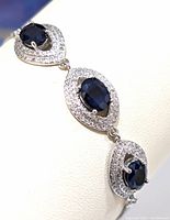 Close-up of silver bracelet segment with an oval blue sapphire surrounded by clear cubic zirconia stones