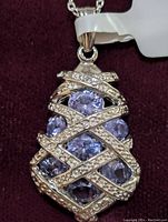 Close-up image showing the front side of pendant with overlapping silver bands set with small CZ stones over faceted light blue tanzanite stones.