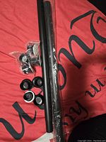 Two black shower rods with mounting brackets and various end caps on red background fabric.