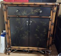 Front view of the bamboo framed stand with drawer and cabinet closed, showing painted bamboo leaf design
