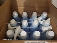 Top view showing 12 bottles of blue cleaner with white caps and spray nozzles neatly arranged in a cardboard box.