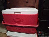 Closed view of rectangular red Coleman cooler with white lid and handle, showing logo on the front and lid design.