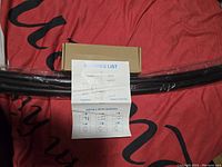 Curved black shower rod laid out on red fabric background with brown packaging box and instruction sheet showing installation steps.