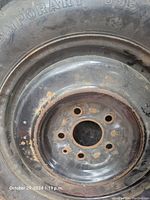Steel rim of temporary donut tire showing 5 bolt holes and surface rust.