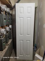 Photo of a brand new six-panel white interior door leaning against a wall next to electric meters.