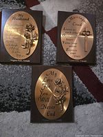 Photo of three plaques on carpet showing sayings and decorations, set in wooden frames with metal oval plates.
