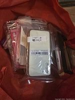 Photo showing multiple Samsung Galaxy S21 Plus phone cases stacked inside an orange bag. Cases are in sealed plastic bags and vary in colors and styles including white, clear, and dark shades.